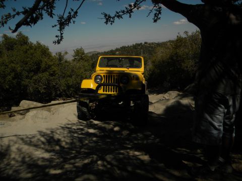 1992 Ford Bronco - A yellow Jeep is parked on a dirt road with trees and hills in the background.