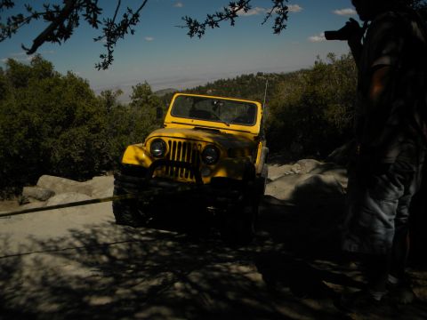 1992 Ford Bronco - A yellow jeep navigates a rocky trail under a clear blue sky.
