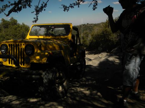 1992 Ford Bronco - A yellow Jeep CJ-7 is parked on a rocky trail under trees, with a person taking a photo.