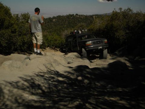 1992 Ford Bronco - A man observes a black Ford Explorer navigating a rocky off-road trail under a clear sky.