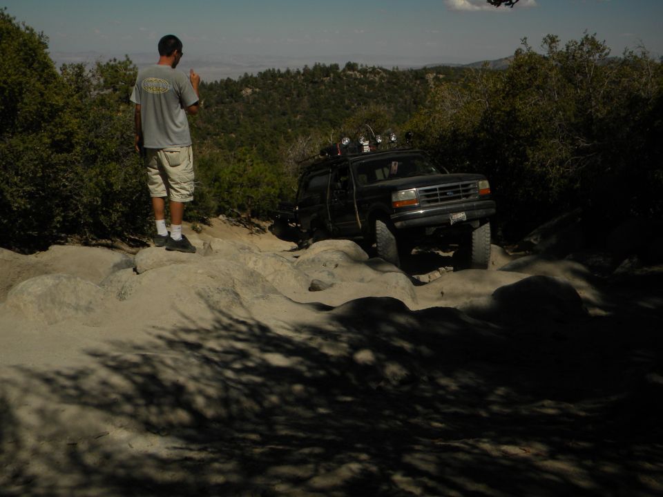Black Ford Explorer climbing over rocks on a trail. A man stands on rocks watching