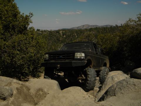 1992 Ford Bronco - A black 1992 Ford Bronco navigates a challenging rocky terrain on a sunny day.