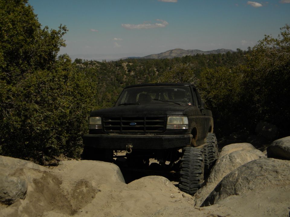 Black Ford pickup truck with large tires navigating rocks on a trail