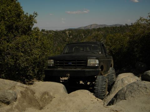 1992 Ford Bronco - A black 1992 Ford Bronco navigates a challenging rocky terrain on a sunny day.
