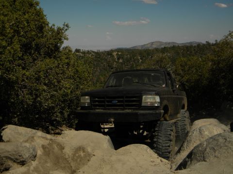 Black 1992 Ford Bronco on a rocky trail with trees and mountains in the background