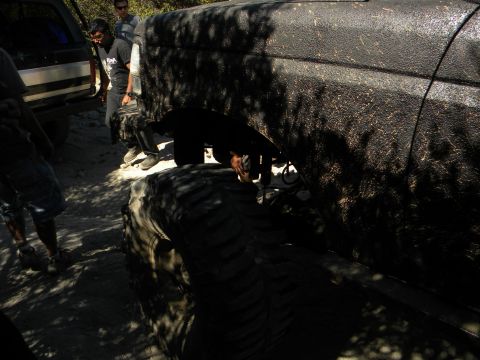 Black 1992 Ford Bronco side view, muddy, with large tires, parked on dirt road