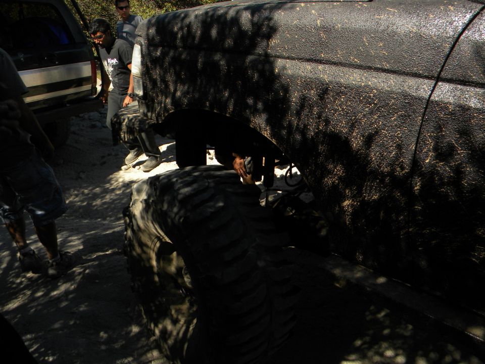 Black 1992 Ford Bronco side view, muddy, with large tires, parked on dirt road