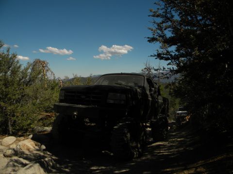 Black pickup truck with large tires on a dirt road, another vehicle visible in the distance