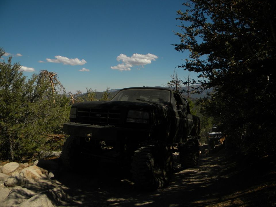 Black pickup truck with large tires on a dirt road, another vehicle visible in the distance