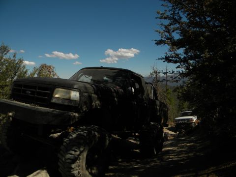Black lifted pickup truck on dirt road, another white truck behind