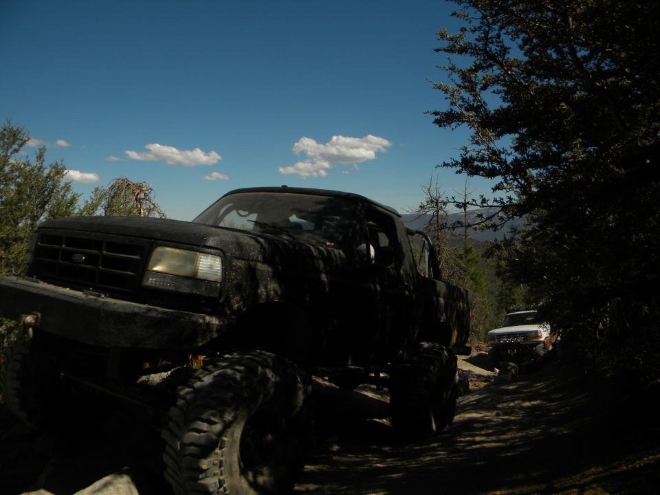Black lifted pickup truck on dirt road, another white truck behind