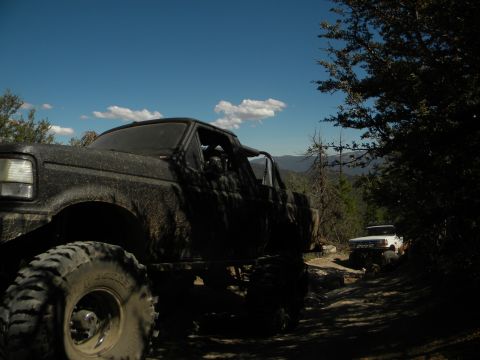 Muddy 1992 Ford Bronco in foreground, white truck on trail behind it