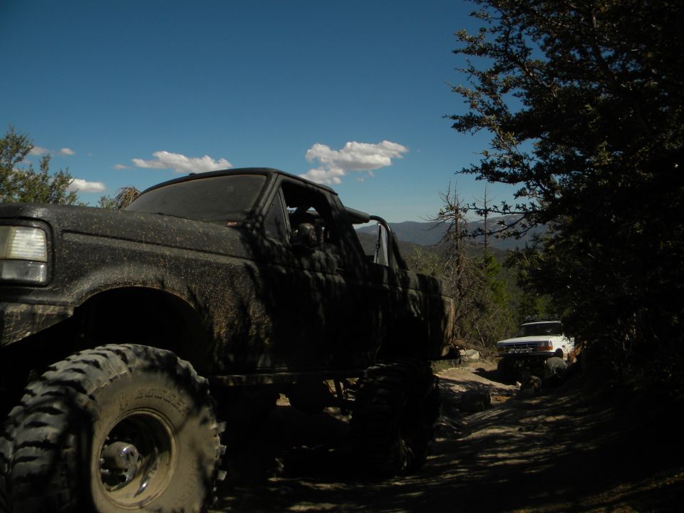 Muddy 1992 Ford Bronco in foreground, white truck on trail behind it