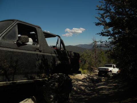 Black 1992 Ford Bronco on a dirt road, side view, with a white Ford truck behind it