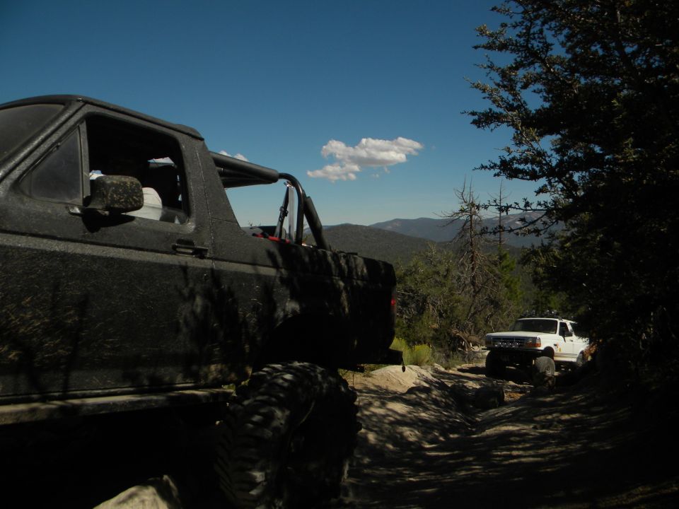 Black 1992 Ford Bronco on a dirt road, side view, with a white Ford truck behind it