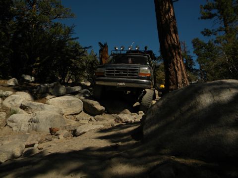 1992 Ford Bronco navigating a boulder-strewn path with trees and clear blue sky
