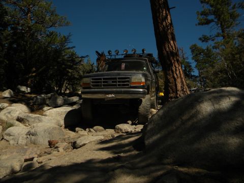 Dark 1992 Ford Bronco on rocky terrain, front view, with roof rack and off-road lights