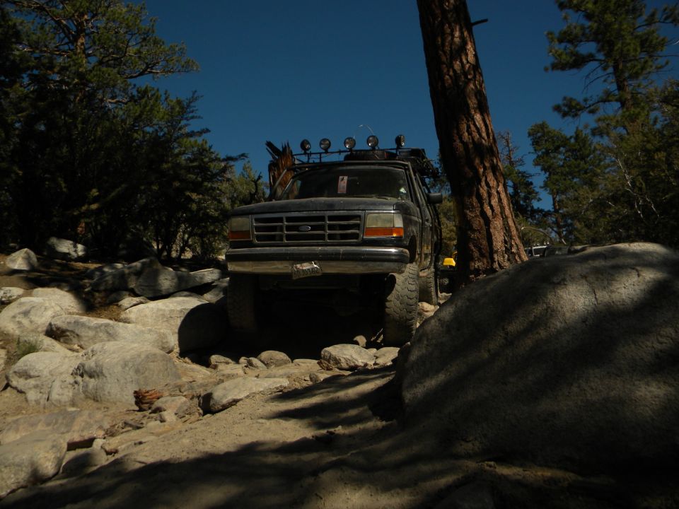 Dark 1992 Ford Bronco on rocky terrain, front view, with roof rack and off-road lights