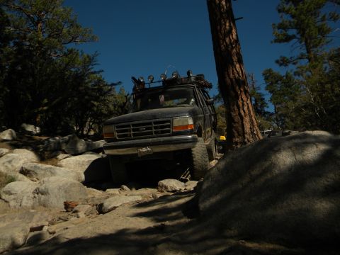Black 1992 Ford Bronco navigating a rocky trail with a roof rack