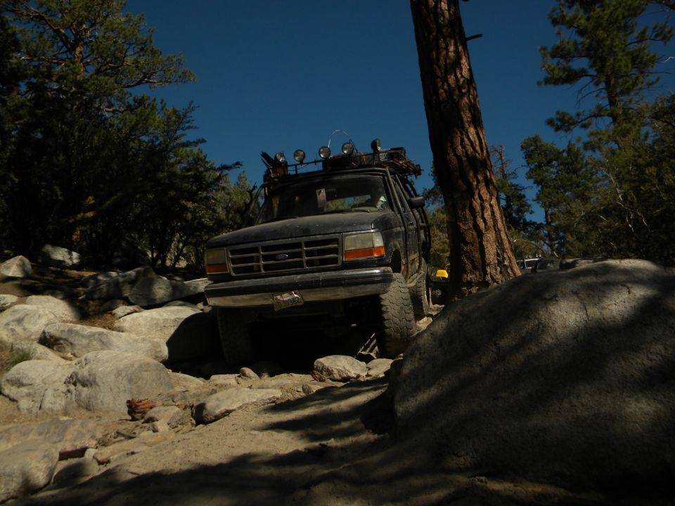 Black 1992 Ford Bronco navigating a rocky trail with a roof rack