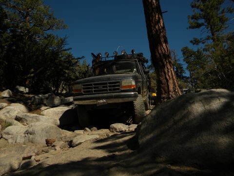 1992 Ford Bronco navigating a rocky trail with trees and blue sky