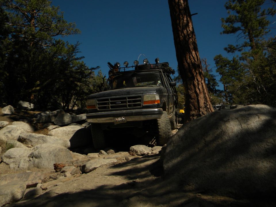 1992 Ford Bronco navigating a rocky trail with trees and blue sky