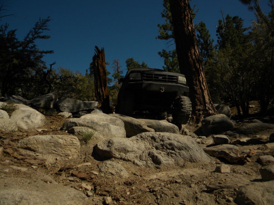 Black 1992 Ford Bronco climbing over large rocks on a wooded trail