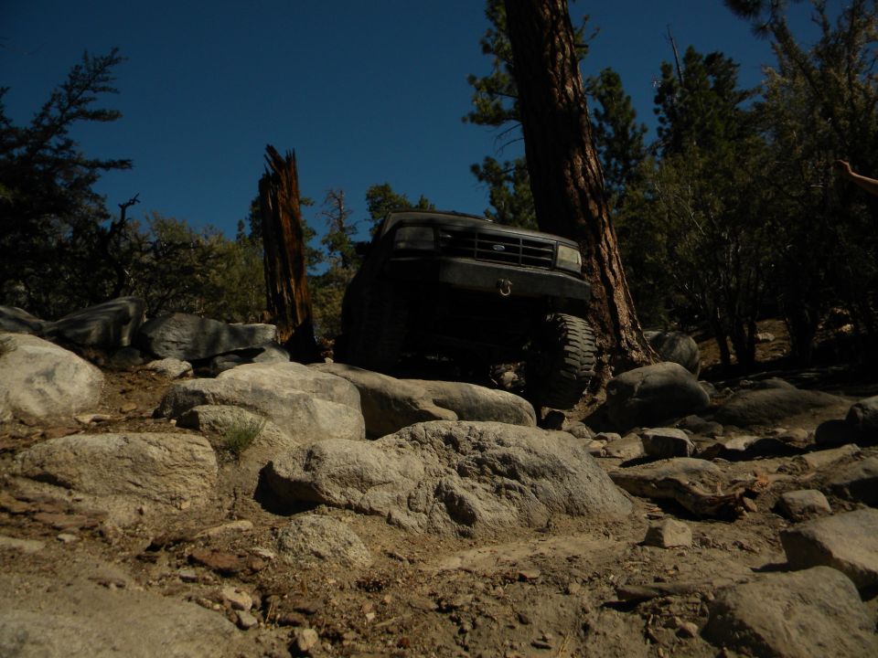 Black 1992 Ford Bronco navigating a rocky, off-road trail with large boulders and trees