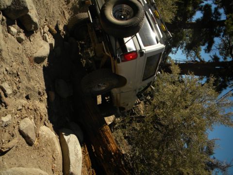 White 1992 Ford Bronco tilted on its side on a rocky, wooded trail
