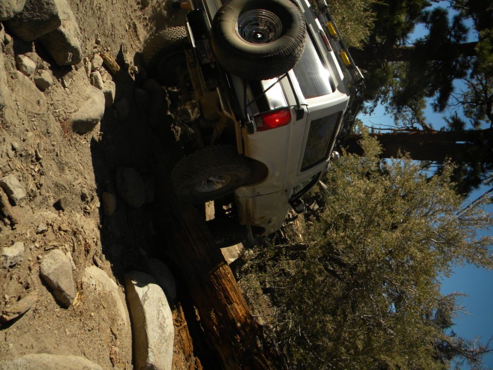 White 1992 Ford Bronco tilted on its side on a rocky, wooded trail
