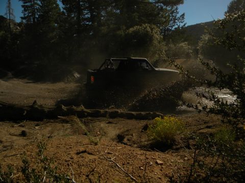 Dark off-road vehicle with roll cage driving through mud and water, kicking up spray