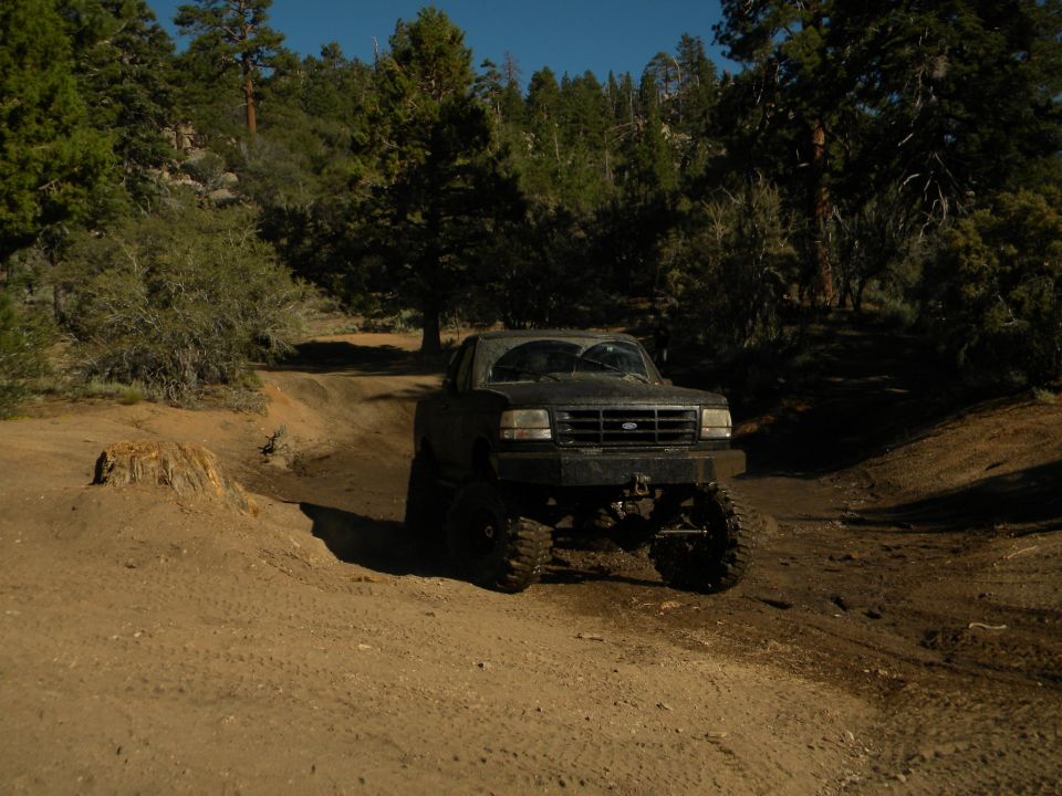 Dark 1992 Ford Bronco on a dirt road, lifted with large tires, front grille visible