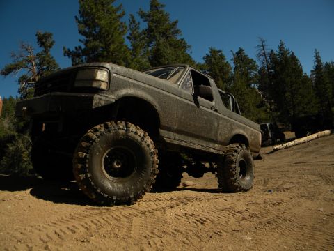 Muddy SUV with large tires on a dirt road, trees in background. Another SUV is visible behind it