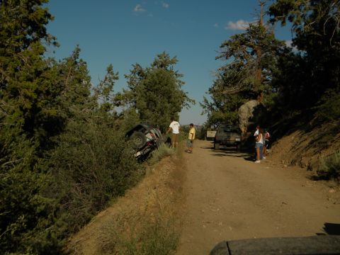 Off-road vehicle overturned on a dirt embankment next to a dirt road with other vehicles and people