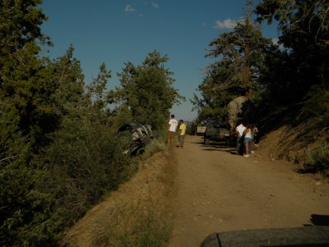 Off-road vehicle tipped into bushes on a dirt road with people standing around