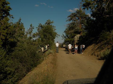 Off-road vehicle tilted on a dirt path with people standing nearby