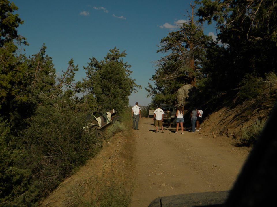 Off-road vehicle on its side on a dirt road with people standing around