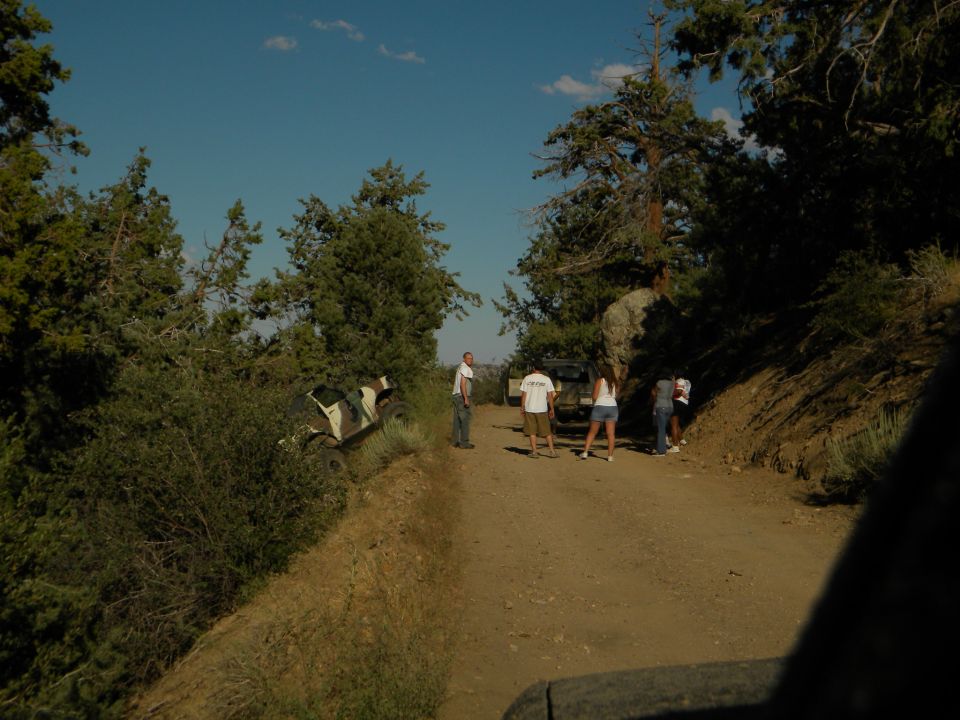 Camouflaged off-road vehicle on dirt road with people nearby