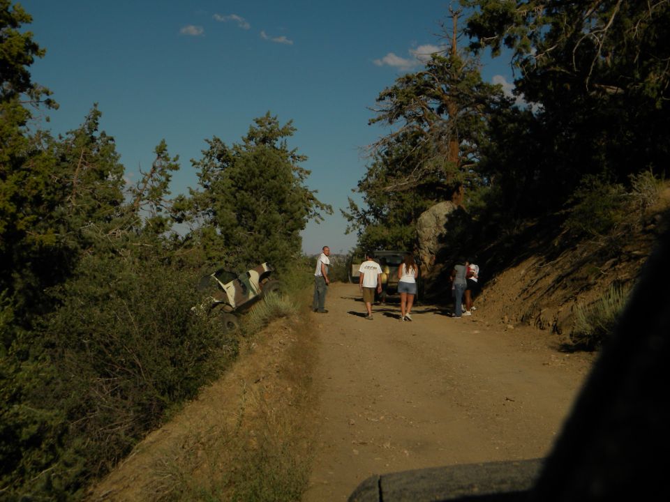 Off-road vehicle tilted in ditch on dirt road, people standing nearby