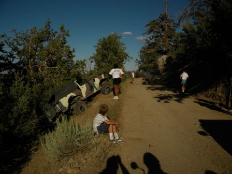 Off-road vehicle tipped on its side on a dirt road with people nearby