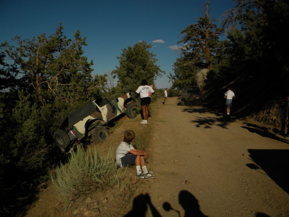 Off-road vehicle tipped on its side on a dirt road with people nearby