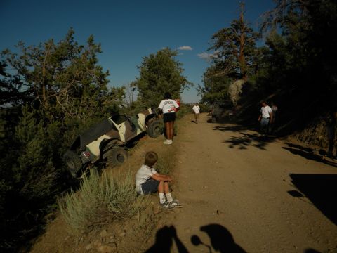 Off-road vehicle tipped on its side on a dirt road with people around
