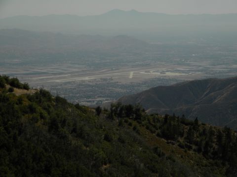View from a mountain overlooking a valley with an airport and distant mountains