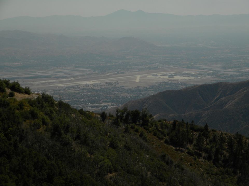 View from a mountain overlooking a valley with an airport and distant mountains