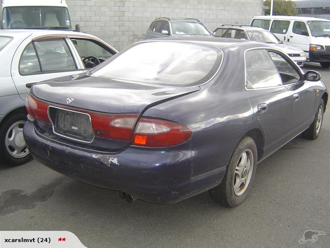 Dark blue Mazda Efini MS-8 sedan rear 3/4 view in salvage yard with damaged bumper