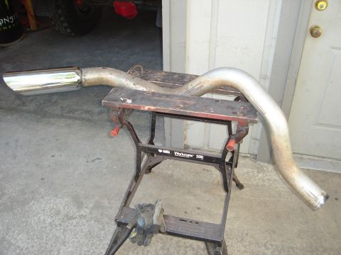 1989 Ford Bronco - A used exhaust pipe with a chrome tip is displayed on a sawhorse in a garage.