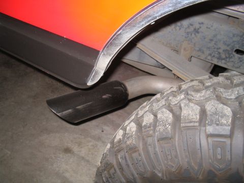 1989 Ford Bronco - The rear tire and exhaust pipe of a vehicle are visible, with a two-tone paint scheme on the body.