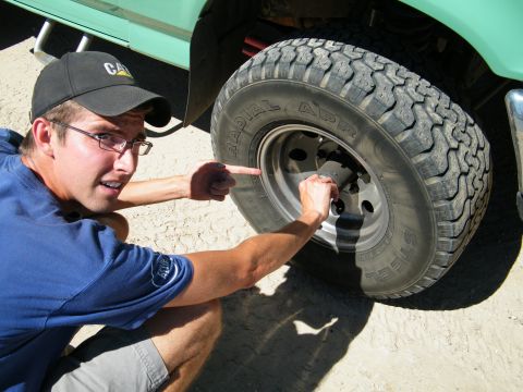 1982 Ford Bronco - A man points to the tire of a green truck, with the Supermotors.net logo visible at the bottom right.