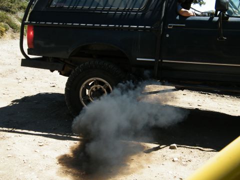 1982 Ford Bronco - A black SUV, possibly from the early 1980s, is seen from the side as it emits a large cloud of black exhaust smoke.