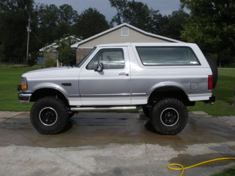 1995 Ford Bronco - This lifted 1995 Ford Bronco features a two-tone paint scheme and aftermarket wheels, presented in a side profile view.